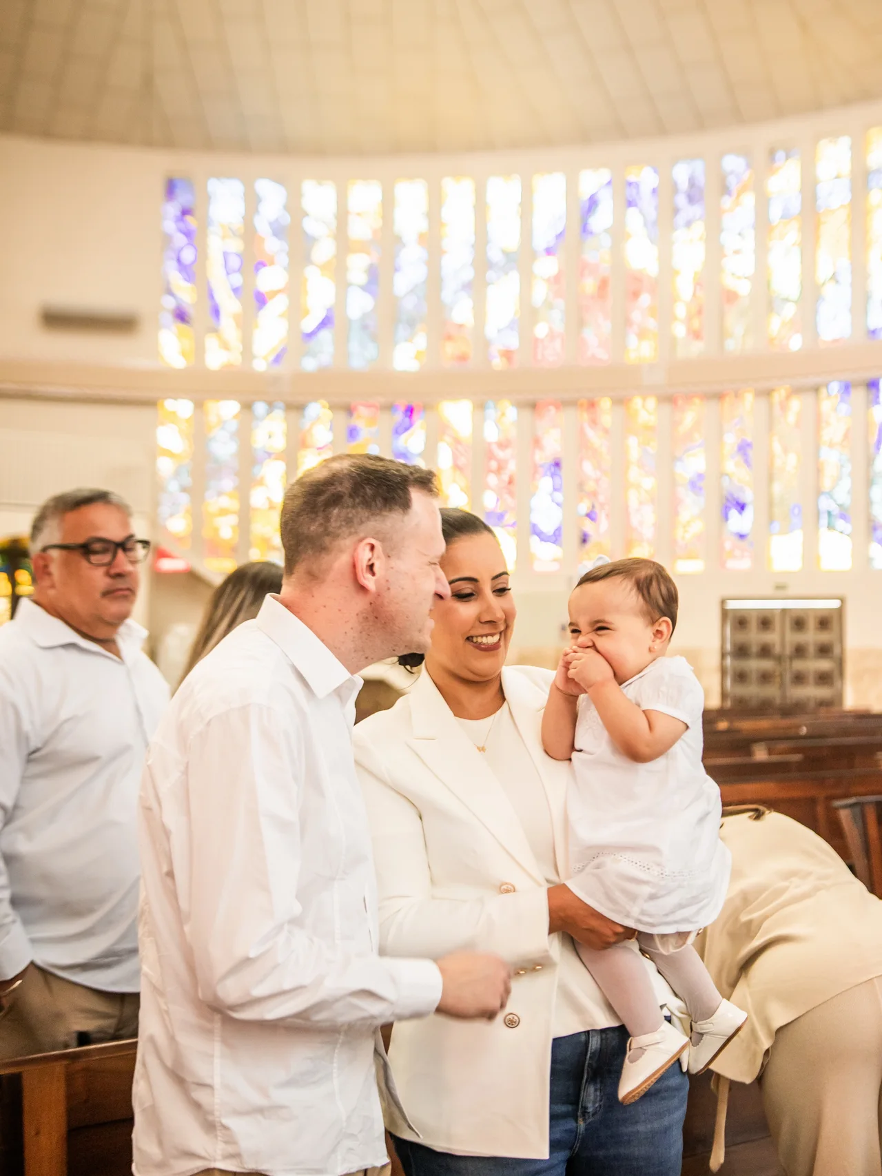 Família com bebê sorrindo durante um batizado.