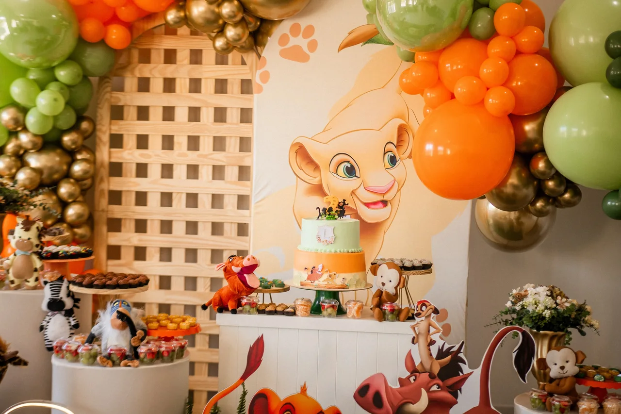 Mesa de bolo com decoração infantil de animais e balões laranja.