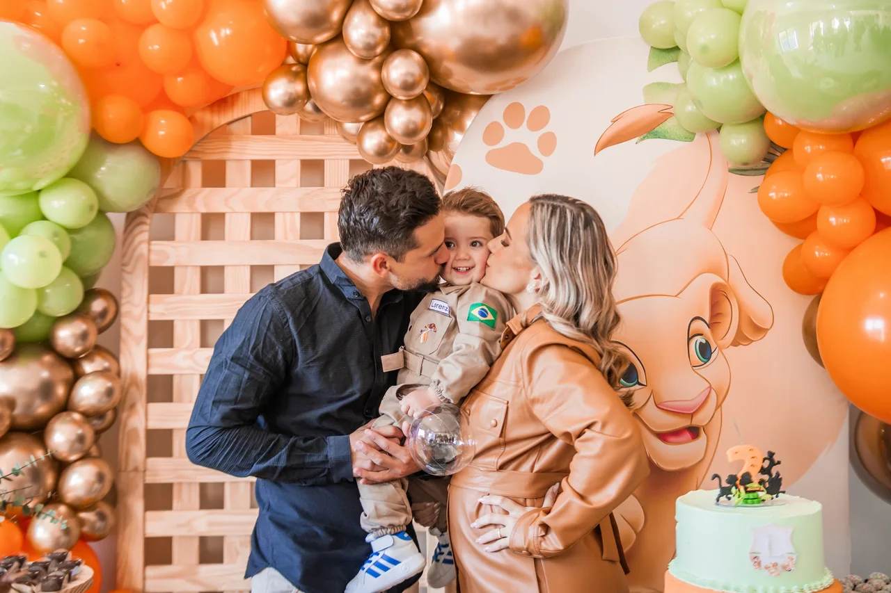 Pais beijam a criança durante um aniversário com decoração de animais.